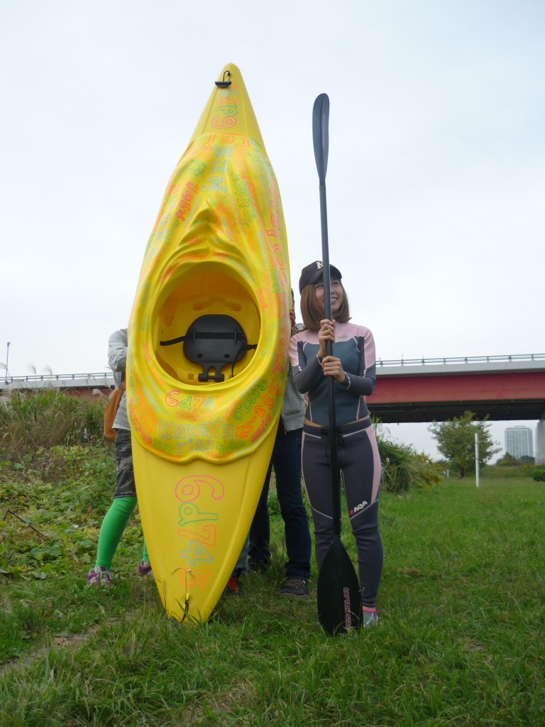 [Figure 1: Rokudenashiko stands by her “man-boat” kayak, whose top attachment was modeled on her vulva, on the banks of the Tamagawa River. (Credit: Taishiro Sakurai)]